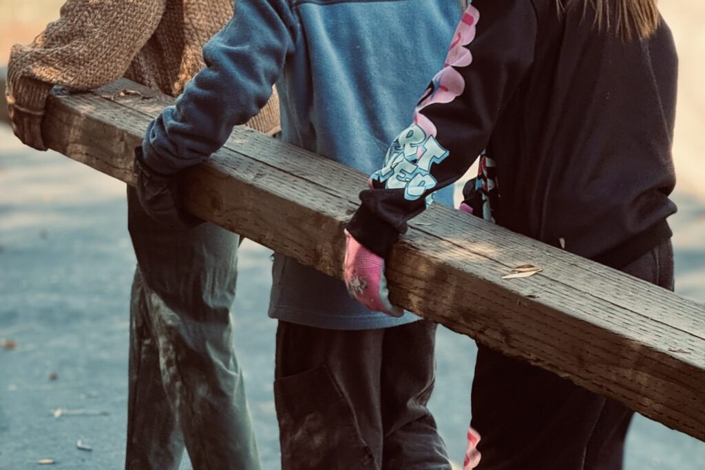 Elementary students working together to carry a wooden beam outdoors